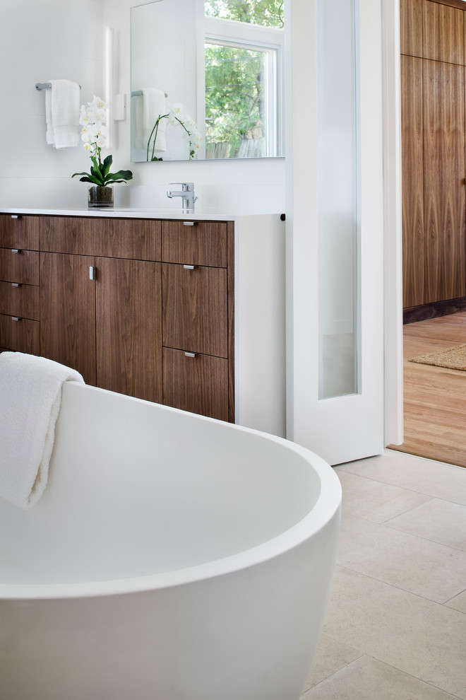 Cette photo montre une grande salle de bain principale tendance en bois foncé avec un placard à porte plane, une baignoire indépendante, un mur blanc, un sol en carrelage de porcelaine, un lavabo encastré et un sol beige.