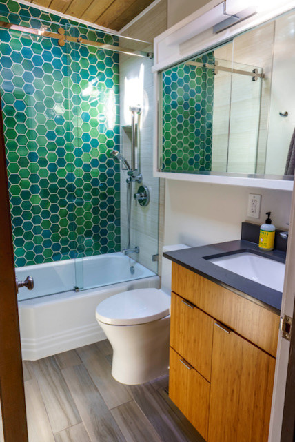 Idées déco pour une salle d'eau rétro en bois brun de taille moyenne avec un placard à porte plane, une baignoire en alcôve, un combiné douche/baignoire, WC à poser, un carrelage vert, un carrelage en pâte de verre, un mur gris, un lavabo encastré, un plan de toilette en surface solide, un sol marron, une cabine de douche à porte coulissante et un plan de toilette noir.