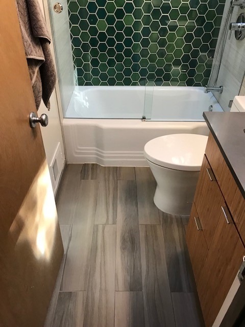 Idéer för att renovera ett mellanstort 50 tals svart svart badrum med dusch, med släta luckor, skåp i mellenmörkt trä, ett badkar i en alkov, en dusch/badkar-kombination, en toalettstol med hel cisternkåpa, grön kakel, glaskakel, grå väggar, ett undermonterad handfat, bänkskiva i akrylsten, brunt golv och dusch med skjutdörr