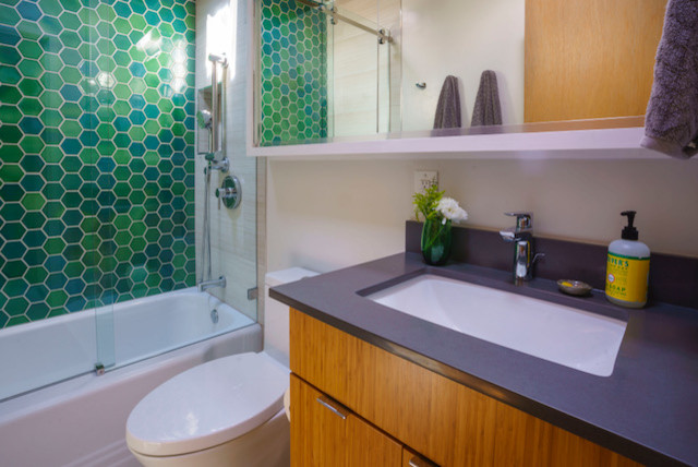 サンフランシスコにある中くらいなミッドセンチュリースタイルのおしゃれなバスルーム (浴槽なし) (フラットパネル扉のキャビネット、中間色木目調キャビネット、アルコーブ型浴槽、シャワー付き浴槽	、一体型トイレ	、緑のタイル、ガラスタイル、グレーの壁、アンダーカウンター洗面器、人工大理石カウンター、茶色い床、引戸のシャワー、黒い洗面カウンター) の写真