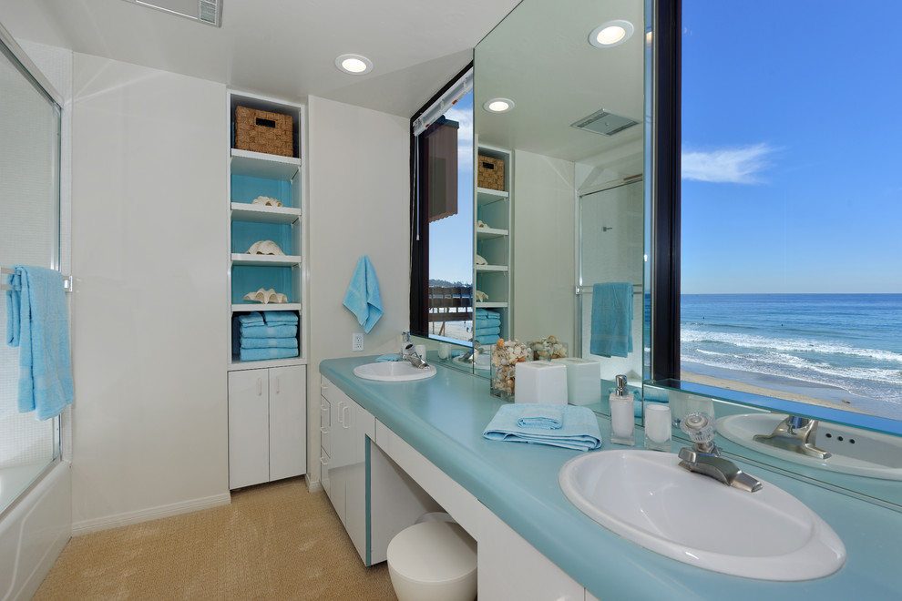 Mittelgroßes Maritimes Badezimmer En Suite mit flächenbündigen Schrankfronten, weißen Schränken, Duschbadewanne, Toilette mit Aufsatzspülkasten, weißer Wandfarbe, Einbauwaschbecken und Mineralwerkstoff-Waschtisch in San Diego