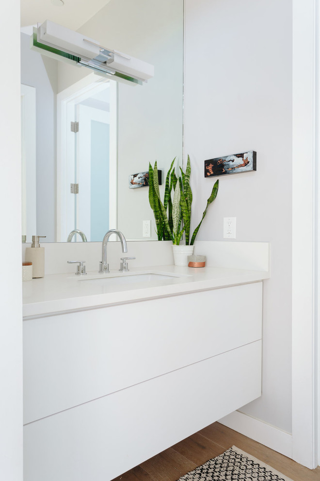 Modernes Badezimmer mit flächenbündigen Schrankfronten, weißen Schränken, grauer Wandfarbe, braunem Holzboden, Unterbauwaschbecken und Quarzwerkstein-Waschtisch in Los Angeles