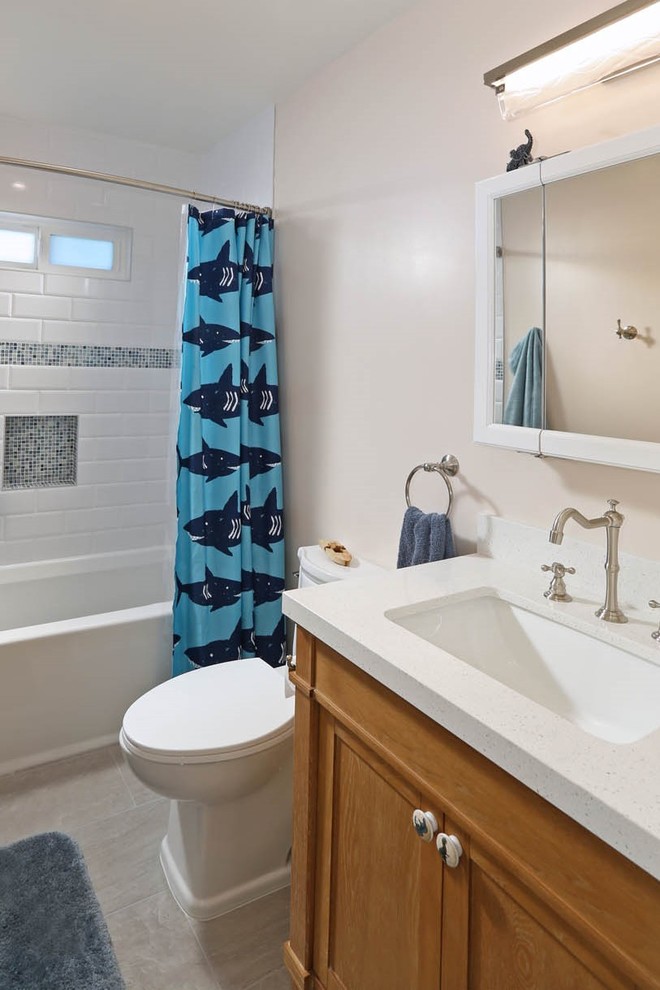Photo of a medium sized nautical family bathroom in Los Angeles with shaker cabinets, medium wood cabinets, an alcove bath, a shower/bath combination, a one-piece toilet, white tiles, metro tiles, beige walls, a submerged sink, grey floors, a shower curtain and engineered stone worktops.