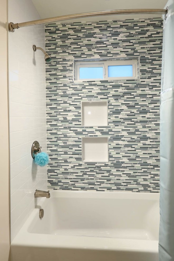 На фото: детская ванная комната среднего размера в морском стиле с фасадами в стиле шейкер, ванной в нише, душем над ванной, унитазом-моноблоком, синей плиткой, бежевыми стенами, врезной раковиной, серым полом, шторкой для ванной, светлыми деревянными фасадами, стеклянной плиткой, полом из керамогранита и столешницей из искусственного кварца с