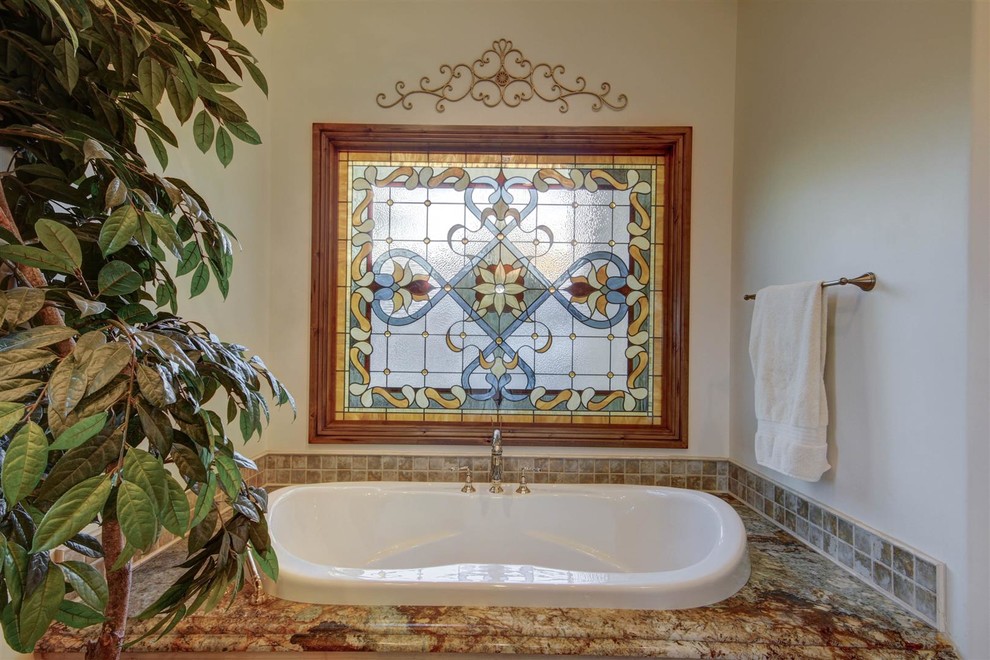 Cette photo montre une grande salle de bain principale méditerranéenne en bois foncé avec un placard à porte affleurante, une baignoire posée, un mur beige, un sol en travertin, un lavabo encastré, un plan de toilette en granite, un sol beige et un plan de toilette multicolore.
