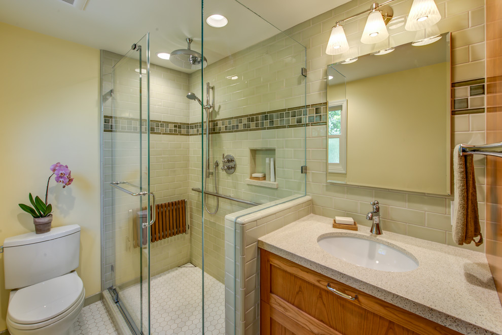 На фото: маленькая ванная комната в классическом стиле с врезной раковиной, фасадами в стиле шейкер, фасадами цвета дерева среднего тона, столешницей из искусственного кварца, угловым душем, раздельным унитазом, зеленой плиткой, керамической плиткой, желтыми стенами, полом из мозаичной плитки, душем с раздвижными дверями, душевой кабиной, белым полом, бежевой столешницей, нишей, сиденьем для душа, тумбой под одну раковину и встроенной тумбой для на участке и в саду
