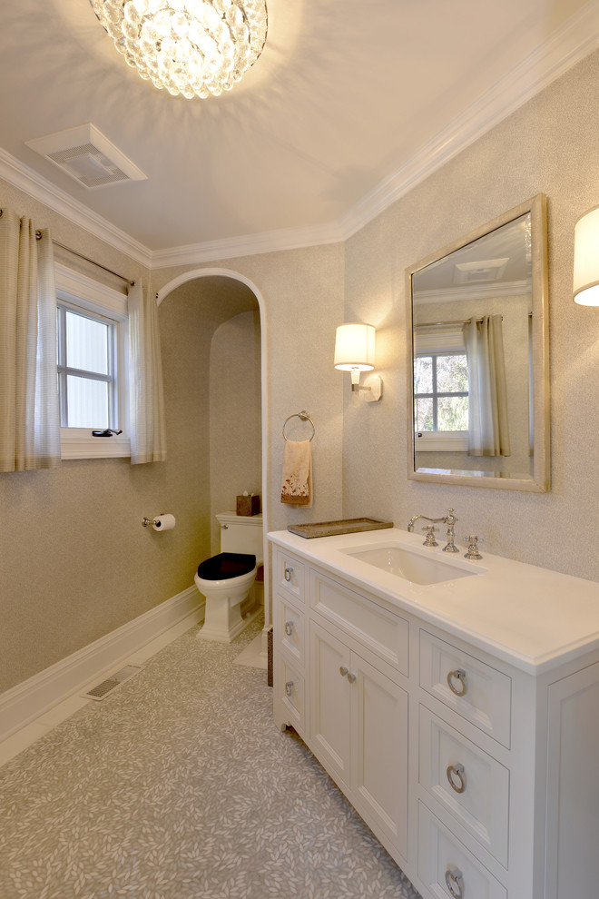 Klassisk inredning av ett en-suite badrum, med ett undermonterad handfat, luckor med infälld panel, vita skåp, en toalettstol med separat cisternkåpa och beige väggar