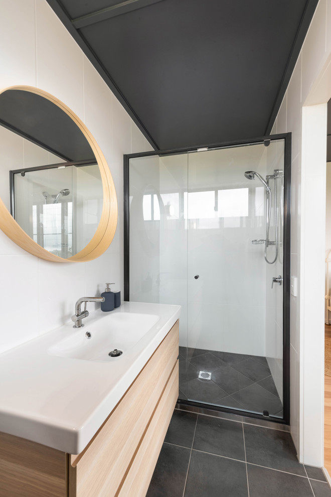 Photo of a small contemporary ensuite bathroom in Sunshine Coast with freestanding cabinets, light wood cabinets, an alcove shower, a one-piece toilet, white tiles, ceramic tiles, white walls, porcelain flooring, an integrated sink, black floors, a hinged door and white worktops.