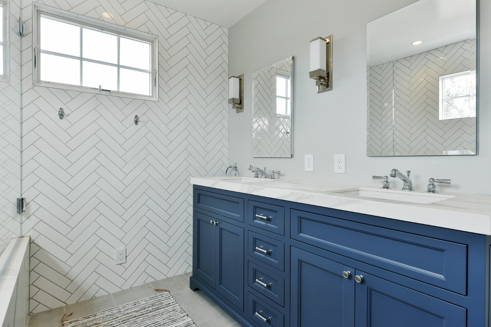 Пример оригинального дизайна: ванная комната среднего размера в стиле неоклассика (современная классика) с фасадами островного типа, синими фасадами, ванной в нише, душем над ванной, белой плиткой, керамической плиткой, серыми стенами, полом из керамогранита, душевой кабиной, врезной раковиной, мраморной столешницей, серым полом, открытым душем и белой столешницей