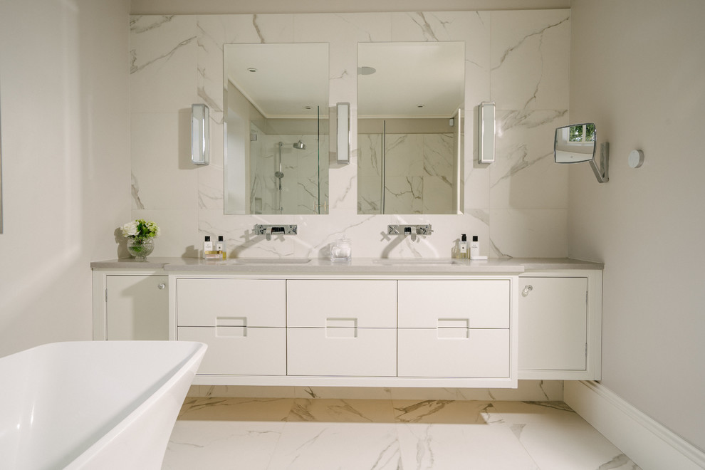 Inspiration pour une grande salle de bain design avec un sol en carrelage de porcelaine, un sol blanc, un plan de toilette blanc, un placard à porte plane, des portes de placard blanches, une baignoire indépendante, un mur gris et un lavabo encastré.