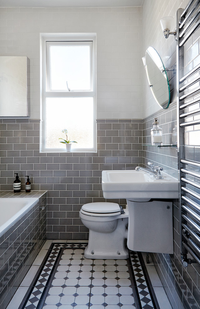 This is an example of a small traditional bathroom in London with glass-front cabinets, a built-in bath, a shower/bath combination, a one-piece toilet, grey tiles, ceramic tiles, grey walls, mosaic tile flooring and a wall-mounted sink.