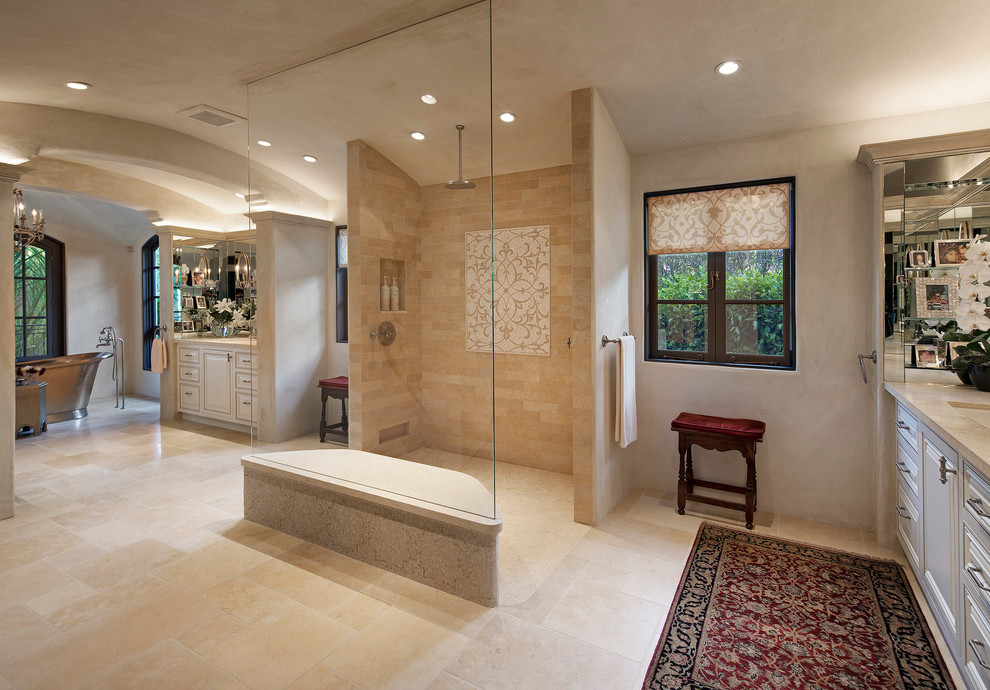 Inspiration for a large mediterranean ensuite bathroom in Santa Barbara with recessed-panel cabinets, beige cabinets, a freestanding bath, a built-in shower, a one-piece toilet, beige tiles, limestone tiles, beige walls, limestone flooring, a submerged sink, limestone worktops, beige floors and an open shower.