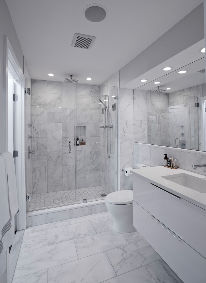 Пример оригинального дизайна: маленькая главная ванная комната в стиле модернизм с плоскими фасадами, белыми фасадами, душем в нише, унитазом-моноблоком, белой плиткой, мраморной плиткой, белыми стенами, мраморным полом, врезной раковиной, столешницей из искусственного кварца, белым полом, душем с распашными дверями и белой столешницей для на участке и в саду