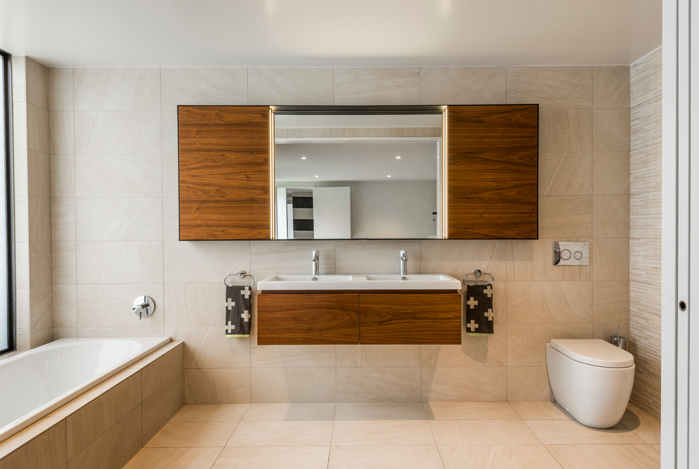 Modernes Badezimmer mit Waschtischkonsole, flächenbündigen Schrankfronten, dunklen Holzschränken, Einbaubadewanne, Toilette mit Aufsatzspülkasten und beigen Fliesen in Sonstige