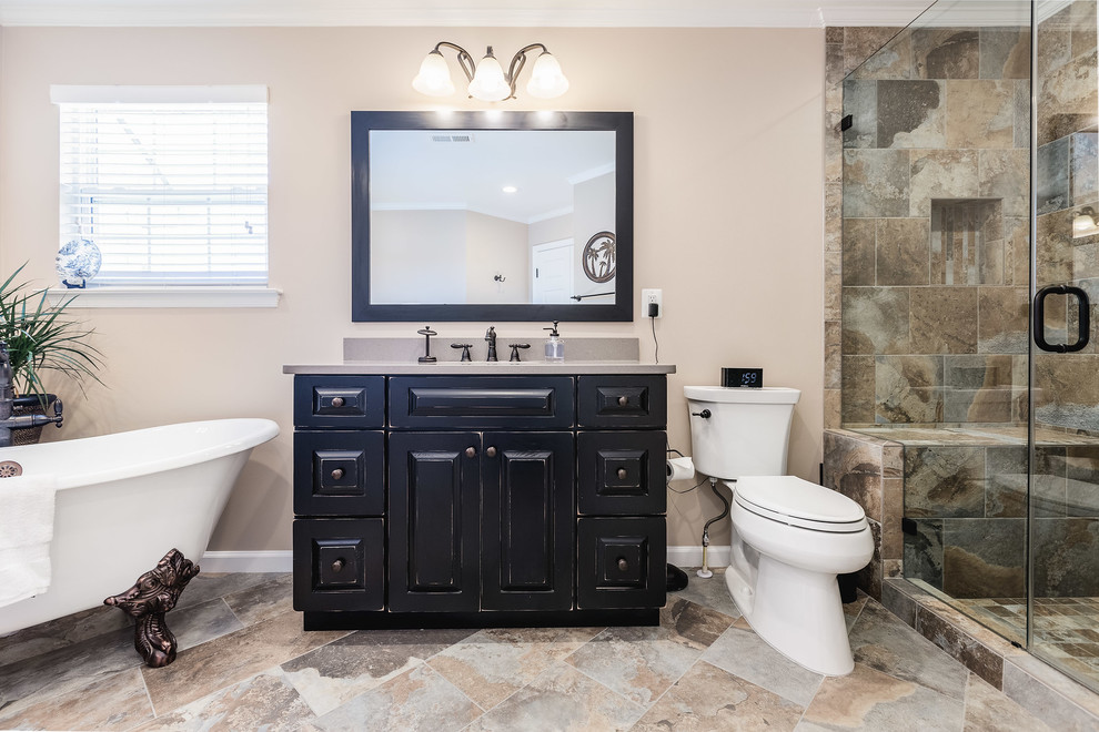 Cette image montre une salle de bain traditionnelle avec un placard avec porte à panneau surélevé, des portes de placard noires, une baignoire sur pieds, WC séparés, un carrelage beige, un carrelage marron, un carrelage gris, un mur beige, un lavabo encastré, un sol multicolore, une cabine de douche à porte battante et un plan de toilette gris.