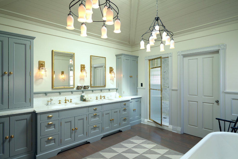 Exemple d'une grande salle de bain principale chic avec un placard à porte affleurante, des portes de placard grises, un sol en vinyl, une baignoire sur pieds, une douche d'angle, un mur beige, un lavabo encastré et un plan de toilette en surface solide.