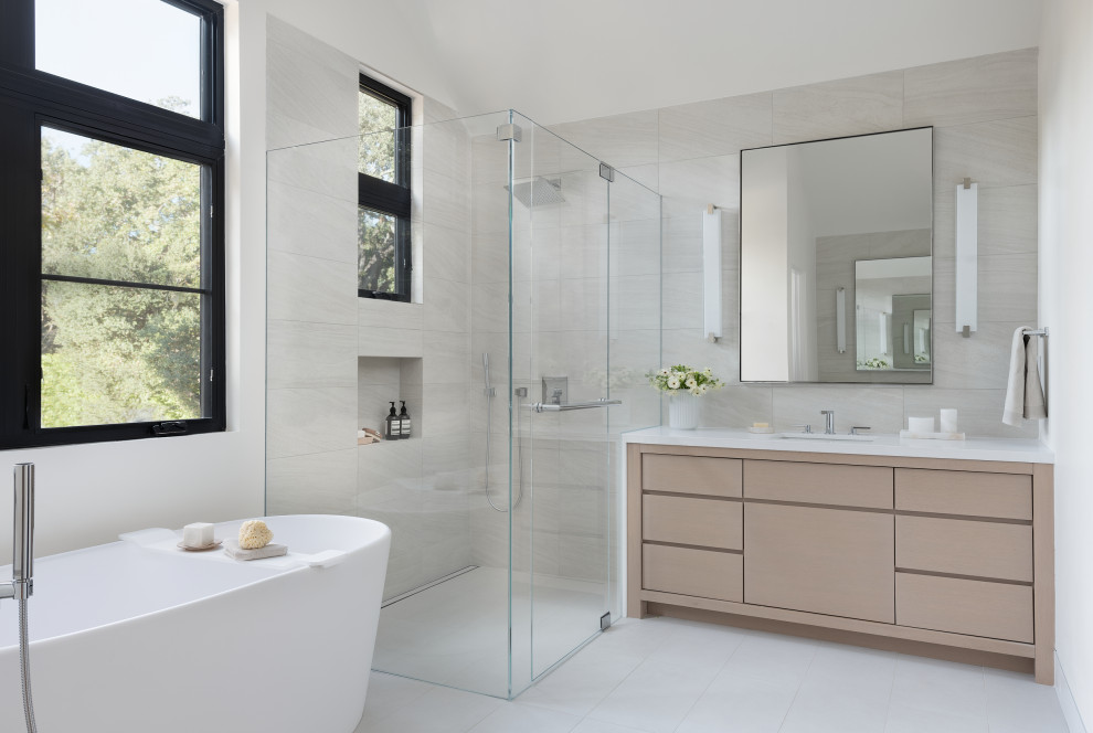 Foto på ett funkis vit badrum, med släta luckor, skåp i ljust trä, ett fristående badkar, en kantlös dusch, grå kakel, ett undermonterad handfat, grått golv och dusch med gångjärnsdörr