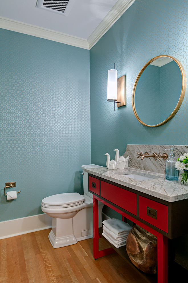 Cette photo montre une petite salle d'eau chic avec WC à poser, un placard en trompe-l'oeil, des portes de placard rouges, un mur bleu, un sol en bois brun, un lavabo encastré et un plan de toilette en marbre.