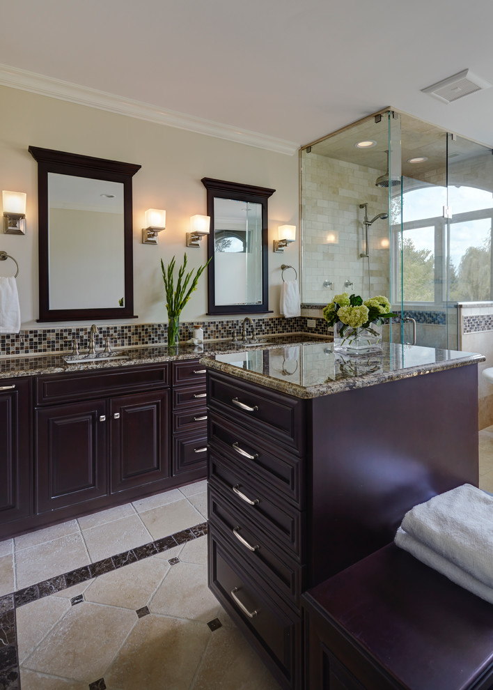 This is an example of a large classic ensuite bathroom in Chicago with a submerged sink, raised-panel cabinets, dark wood cabinets, marble worktops, a freestanding bath, a corner shower, beige tiles, stone tiles, beige walls and travertine flooring.