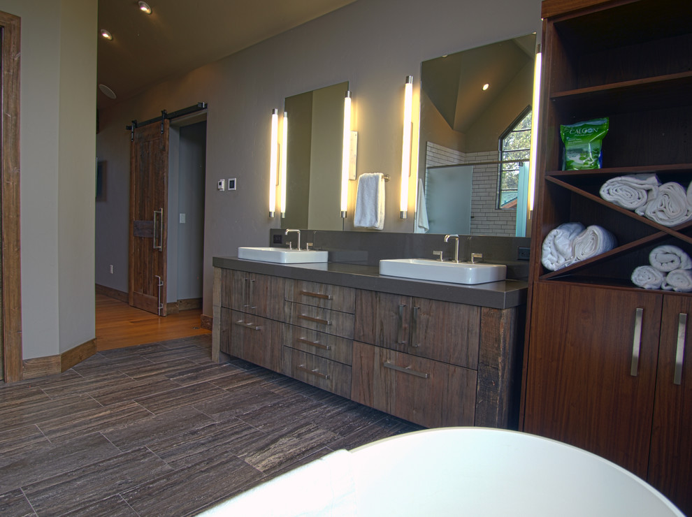 Modern inredning av ett stort en-suite badrum, med släta luckor, skåp i mörkt trä, ett fristående badkar, en dusch i en alkov, grå väggar, korkgolv, ett nedsänkt handfat, bänkskiva i betong, brunt golv och dusch med gångjärnsdörr