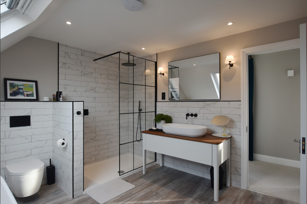 Modern inredning av ett vit vitt badrum, med släta luckor, vita skåp, en hörndusch, vit kakel, grå väggar, mellanmörkt trägolv, ett fristående handfat, brunt golv och med dusch som är öppen