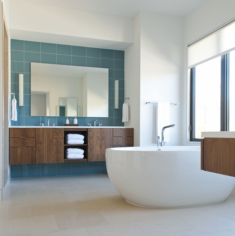 Exempel på ett modernt badrum, med släta luckor, skåp i mörkt trä, ett fristående badkar och blå kakel