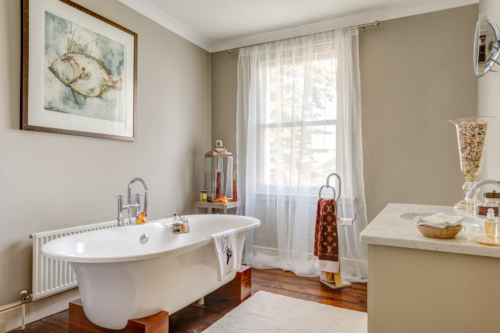 Immagine di una grande stanza da bagno chic con lavabo integrato, consolle stile comò, ante beige, top in granito, vasca freestanding, pareti beige e pavimento in legno massello medio