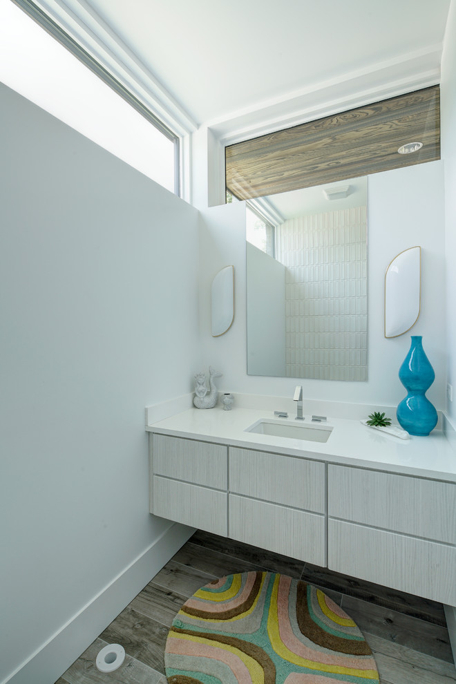 Modelo de cuarto de baño actual de tamaño medio con armarios con paneles lisos, puertas de armario blancas, paredes blancas, suelo de madera en tonos medios, lavabo bajoencimera, encimera de acrílico y suelo gris