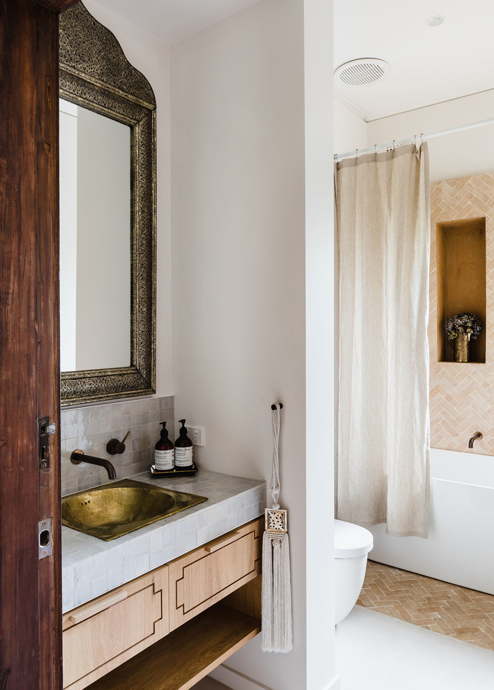 Стильный дизайн: ванная комната в средиземноморском стиле с плоскими фасадами, светлыми деревянными фасадами, ванной в нише, душем над ванной, унитазом-моноблоком, бежевой плиткой, бежевыми стенами, душевой кабиной, накладной раковиной, серым полом и серой столешницей - последний тренд