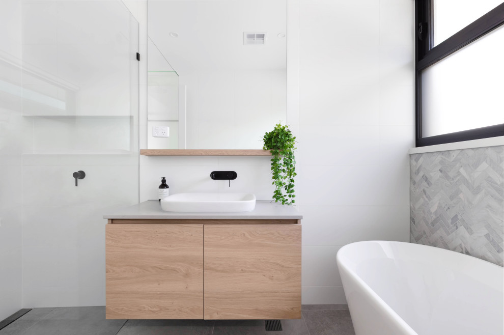Modernes Badezimmer mit flächenbündigen Schrankfronten, hellen Holzschränken, freistehender Badewanne, Duschnische, grauen Fliesen, Mosaikfliesen, Aufsatzwaschbecken, grauem Boden, grauer Waschtischplatte, Einzelwaschbecken und schwebendem Waschtisch in Melbourne