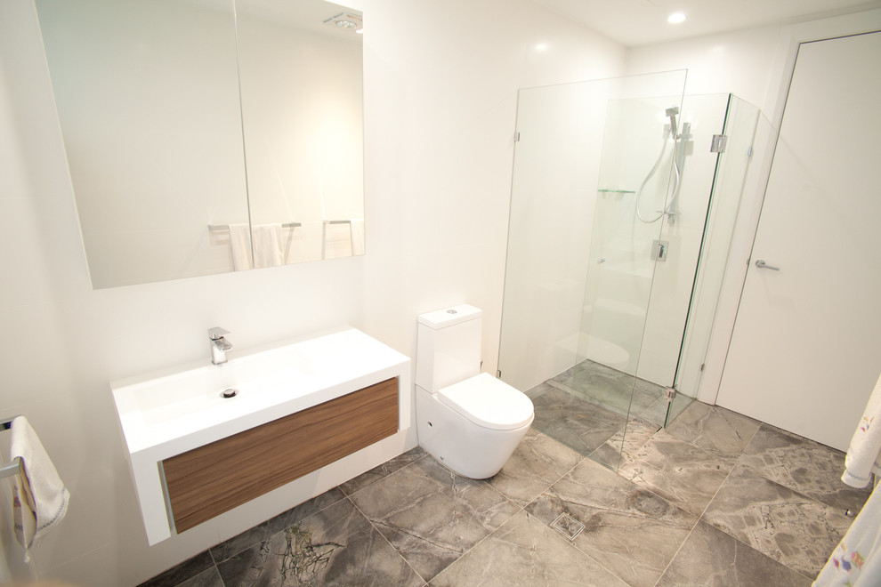 Ispirazione per una piccola stanza da bagno moderna con lavabo integrato, ante di vetro, top in superficie solida, doccia ad angolo, WC monopezzo, piastrelle grigie, piastrelle in pietra e pareti bianche