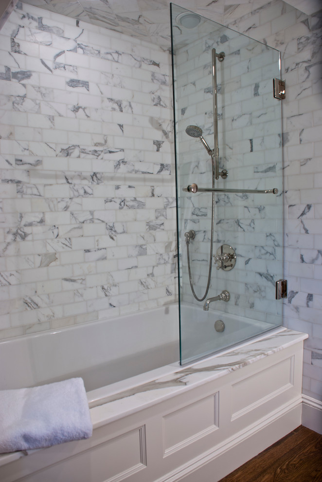 Cette image montre une salle de bain principale traditionnelle de taille moyenne avec un lavabo encastré, un plan de toilette en marbre, une baignoire encastrée, un combiné douche/baignoire, WC à poser, un carrelage blanc, un carrelage de pierre, un mur beige et parquet foncé.