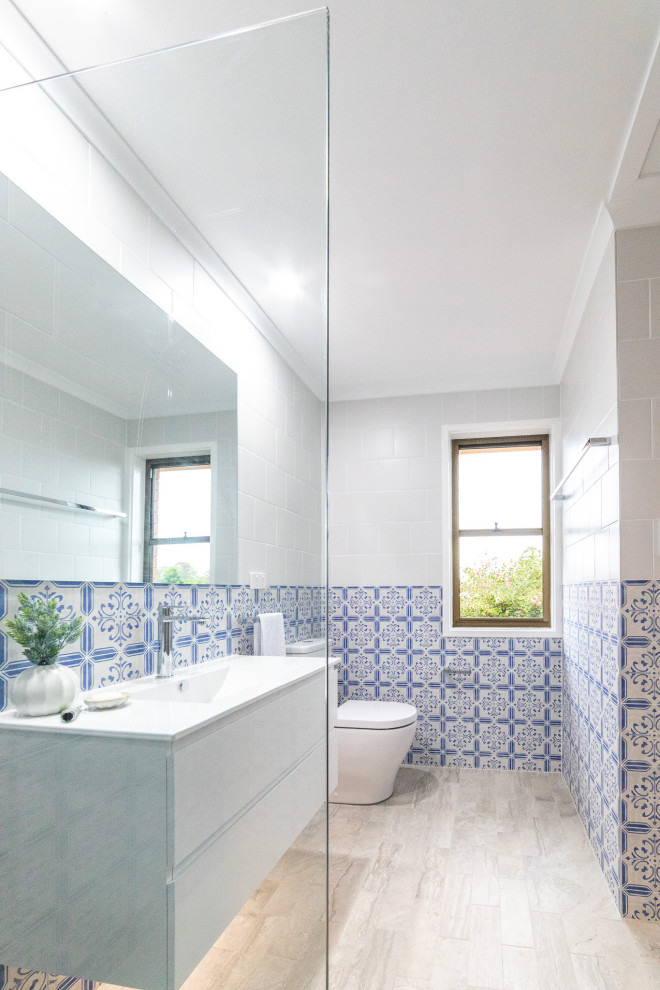 Идея дизайна: ванная комната среднего размера в стиле модернизм с плоскими фасадами, белыми фасадами, открытым душем, унитазом-моноблоком, разноцветной плиткой, керамической плиткой, разноцветными стенами, полом из керамогранита, душевой кабиной, монолитной раковиной, разноцветным полом, открытым душем, белой столешницей, нишей, тумбой под одну раковину и подвесной тумбой
