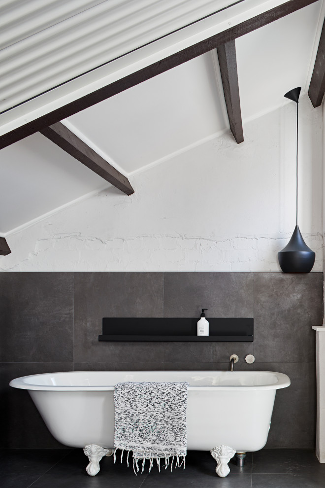 Inspiration pour une salle de bain principale urbaine avec une baignoire sur pieds, un carrelage gris, un mur blanc, un sol gris, poutres apparentes et un plafond voûté.