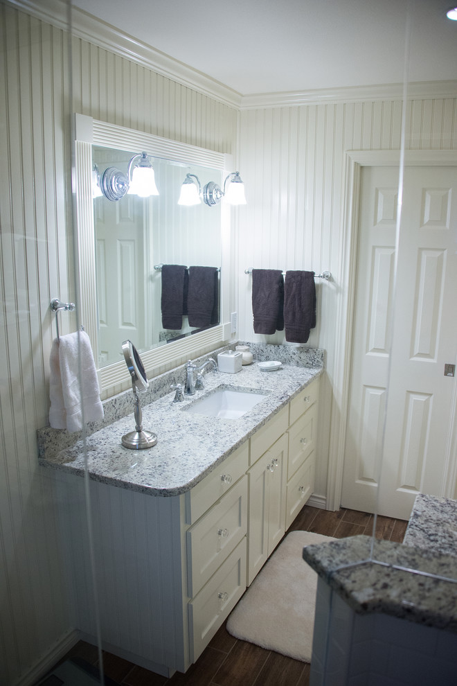 Klassisk inredning av ett badrum, med ett undermonterad handfat, luckor med infälld panel, vita skåp, granitbänkskiva, en toalettstol med hel cisternkåpa, vit kakel, gula väggar och klinkergolv i keramik