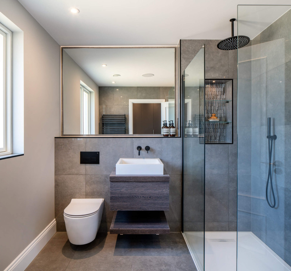 Exempel på ett mellanstort modernt grå grått badrum med dusch, med släta luckor, skåp i mörkt trä, en hörndusch, en vägghängd toalettstol, grå kakel, grå väggar, ett fristående handfat, grått golv och med dusch som är öppen