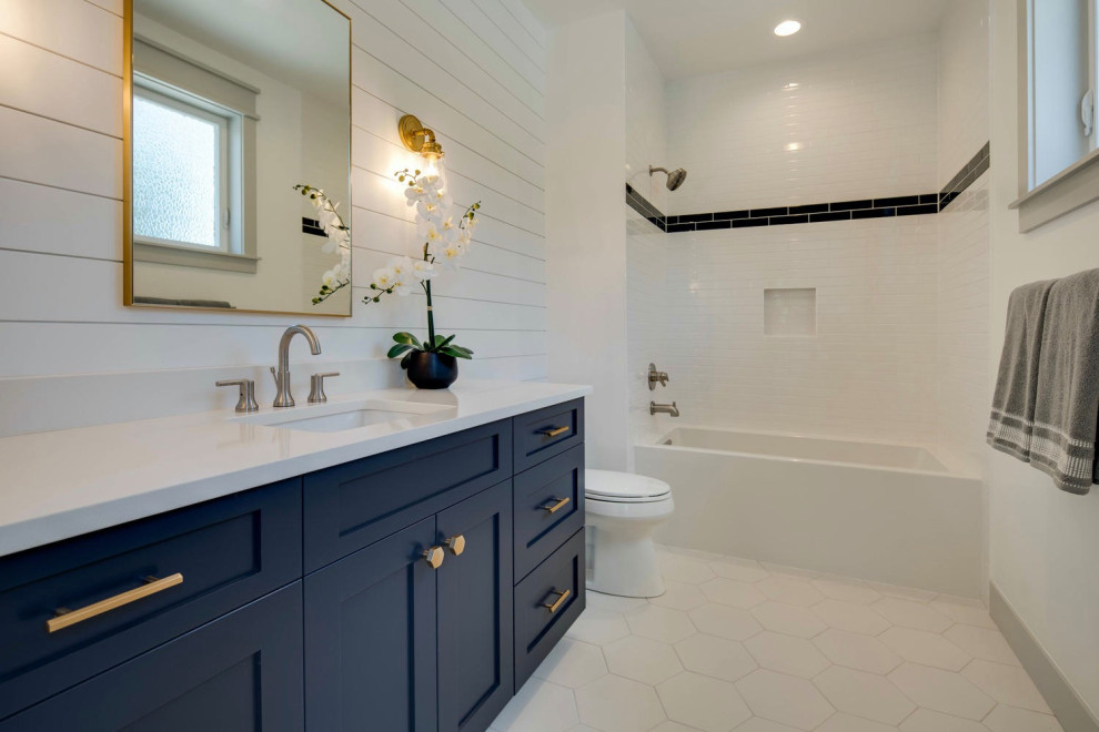 Inspiration for a medium sized classic family bathroom in Denver with shaker cabinets, blue cabinets, an alcove bath, a shower/bath combination, white tiles, ceramic tiles, white walls, porcelain flooring, a submerged sink, engineered stone worktops, white floors, white worktops, a wall niche, a single sink, a built in vanity unit and tongue and groove walls.