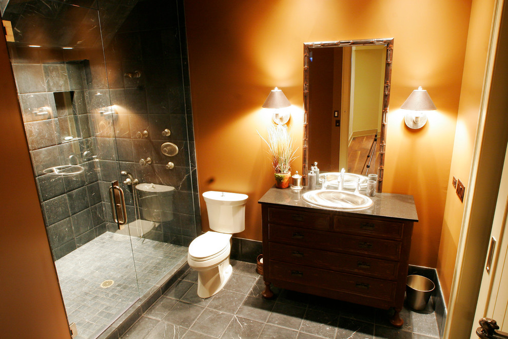 Diseño de cuarto de baño rural con armarios tipo mueble, puertas de armario de madera oscura, encimera de granito y parades naranjas