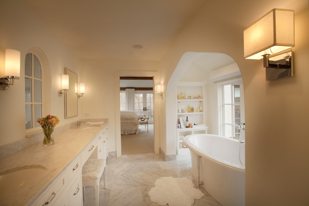 Modelo de cuarto de baño tradicional con lavabo bajoencimera, armarios con paneles empotrados, puertas de armario blancas y bañera exenta