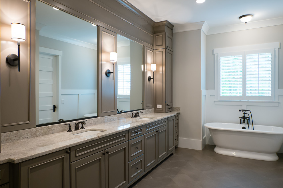 Expansive farmhouse ensuite bathroom in Charlotte with a submerged sink, recessed-panel cabinets, granite worktops, a freestanding bath, a two-piece toilet, grey tiles, porcelain tiles, grey walls, porcelain flooring and grey cabinets.