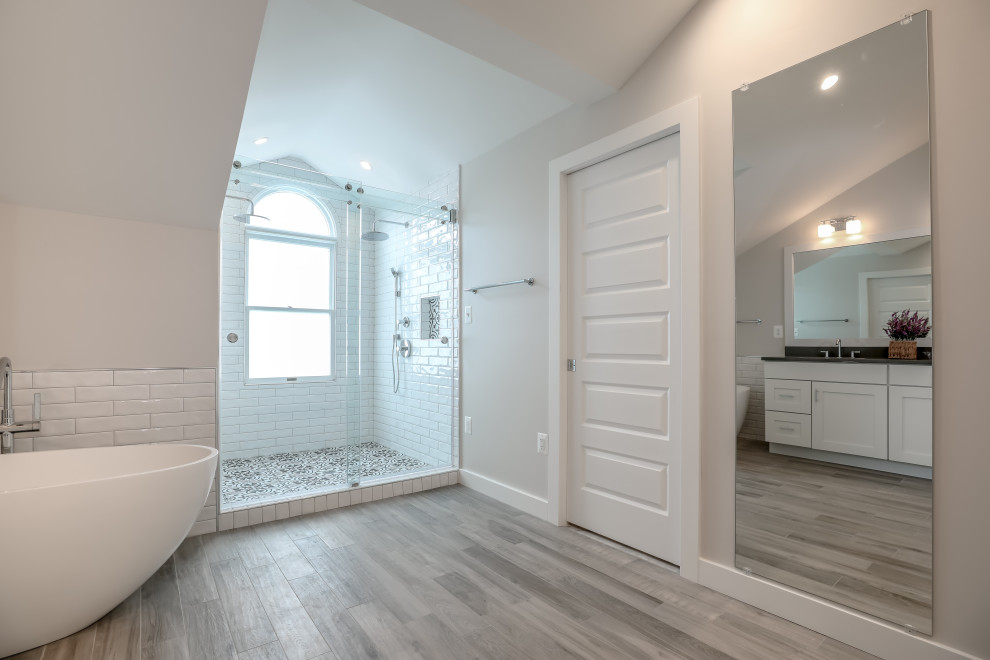Cette photo montre une salle de bain principale tendance de taille moyenne avec des portes de placard blanches, une baignoire indépendante, une douche double, un carrelage blanc, des carreaux de céramique, un mur beige, un plan de toilette en granite et un plan de toilette noir.