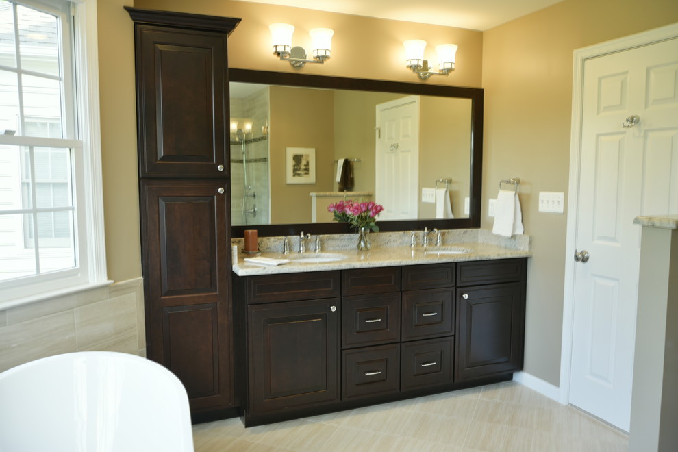 This is an example of a contemporary bathroom in DC Metro with brown cabinets, a freestanding bath, a corner shower, a one-piece toilet, beige tiles, ceramic tiles, beige walls, ceramic flooring, granite worktops, beige floors and beige worktops.