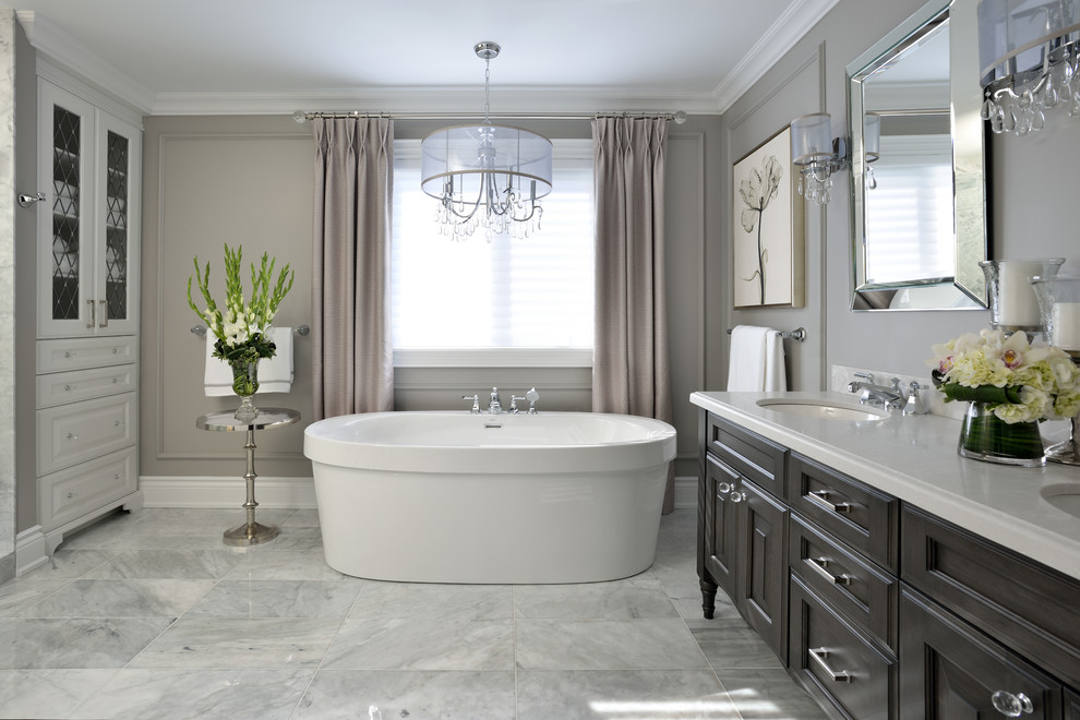 Inspiration for a mid-sized contemporary master white tile marble floor freestanding bathtub remodel in Toronto with raised-panel cabinets, dark wood cabinets, a one-piece toilet, gray walls and an undermount sink