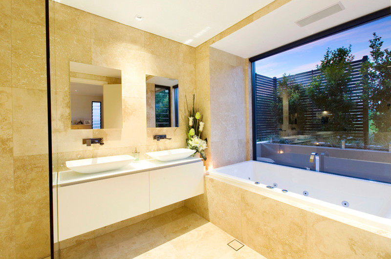 Inspiration for a medium sized contemporary bathroom in Sydney with a vessel sink, flat-panel cabinets, white cabinets, glass worktops, a built-in bath, a walk-in shower, a wall mounted toilet, beige tiles, stone tiles, beige walls and travertine flooring.