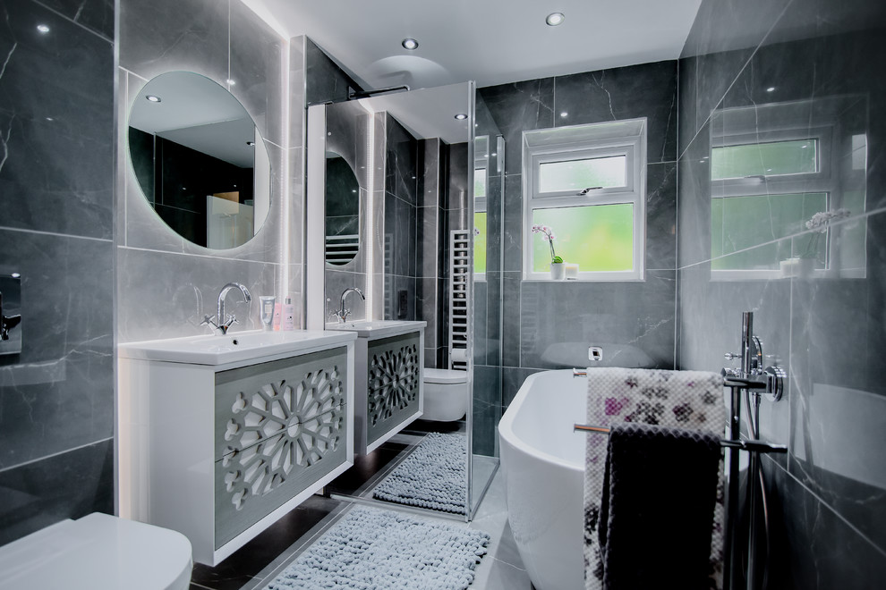 Medium sized contemporary ensuite wet room bathroom in Manchester with light wood cabinets, a freestanding bath, a wall mounted toilet, grey tiles, ceramic tiles, grey walls, porcelain flooring, a wall-mounted sink, grey floors and a hinged door.