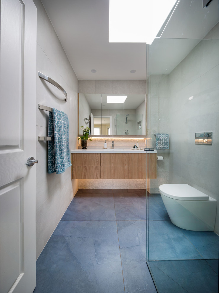 This is an example of a medium sized contemporary ensuite bathroom in Melbourne with freestanding cabinets, medium wood cabinets, a built-in shower, a wall mounted toilet, white tiles, porcelain tiles, white walls, porcelain flooring, a submerged sink, engineered stone worktops, blue floors and a hinged door.
