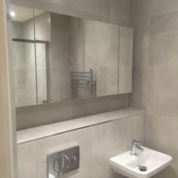 Foto på ett mellanstort funkis en-suite badrum, med en kantlös dusch, en vägghängd toalettstol, grå kakel, keramikplattor, grå väggar, klinkergolv i keramik, ett väggmonterat handfat och kaklad bänkskiva
