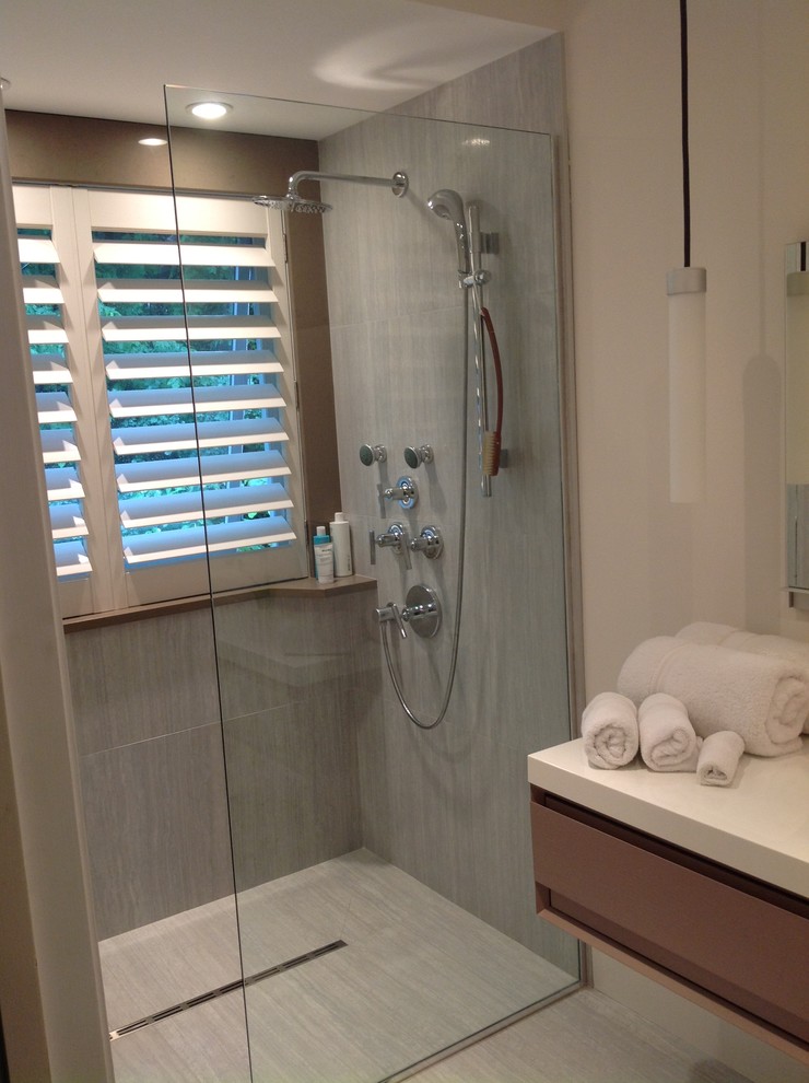 Modernes Badezimmer mit integriertem Waschbecken, flächenbündigen Schrankfronten, grauen Schränken, Mineralwerkstoff-Waschtisch, bodengleicher Dusche, Toilette mit Aufsatzspülkasten, grauen Fliesen und Porzellanfliesen in Montreal