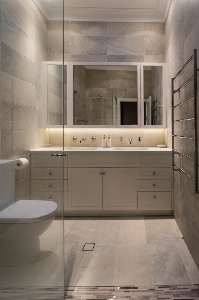 Cette photo montre une salle de bain chic avec des portes de placard blanches, WC à poser, un carrelage gris et un plan de toilette blanc.