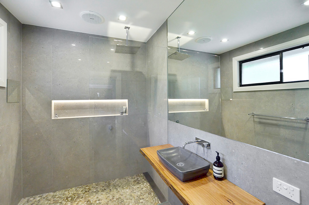 Diseño de cuarto de baño actual pequeño con armarios con paneles lisos, sanitario de pared, baldosas y/o azulejos grises, suelo de baldosas tipo guijarro, encimera de madera y ducha abierta